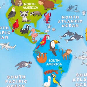 May include: A colorful world map with illustrations of animals from different continents. The map includes North America, South America, North Atlantic Ocean, South Pacific Ocean, and South Atlantic Ocean. The map is on a blue background.