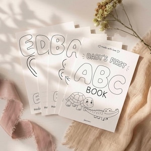 May include: A stack of white paper coloring pages titled Baby's First ABC Book, featuring black line art of a turtle and a crocodile on the cover. The pages include large bubble letters and the text made with love at the top and bottom.