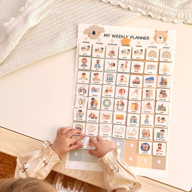 May include: A child's weekly planner with a koala and bear design. The planner features illustrated activity icons for each day of the week. The text "MY WEEKLY PLANNER" is at the top. The child's hands are interacting with the planner.