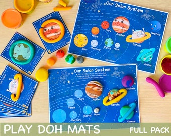 May include: A set of blue and white play dough mats featuring a solar system theme. The mats have illustrations of the planets and the sun, with space for children to create their own planets using play dough. The mats are labeled "Our Solar System" and "Play Doh Mats".