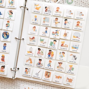 May include: A white binder filled with square cards featuring colorful illustrations of daily activities. The cards include images and text such as "Dad Comes Home," "Feed Animals," and "Take Out Garbage." The binder is open, displaying multiple rows of the cards.