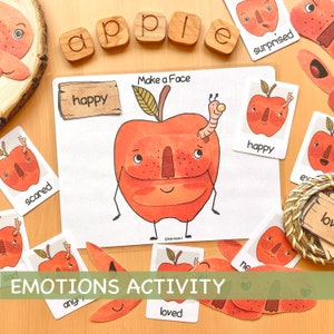 May include: A printable emotions activity for children featuring a red apple with different facial expressions. The activity includes a set of cards with various emotions, such as happy, sad, scared, and loved. The cards are designed to be cut out and used to create different facial expressions on the apple.