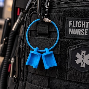 May include: A bright blue cable keychain ring with a screw-lock mechanism, holding two matching blue plastic caps. The keychain is attached to a black tactical backpack featuring a patch with the text FLIGHT NURSE and a medical star symbol.