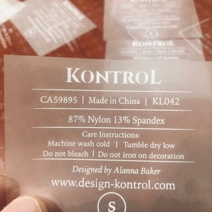 Puede incluir: Una etiqueta blanca con texto negro que dice "KONTROL CA59895 | Made in China | KL042 87% Nylon 13% Spandex Instrucciones de cuidado: Lavar a máquina con agua fría | Secar en secadora a baja temperatura No usar lejía | No planchar sobre la decoración Diseñado por Alanna Baker www.design-kontrol.com S".