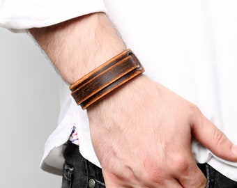 May include: A brown leather bracelet with a distressed finish. The bracelet is worn on a person's wrist.