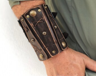 May include: A brown leather cuff bracelet with decorative stitching and brass accents. The bracelet has a distressed look and is fastened with a buckle.