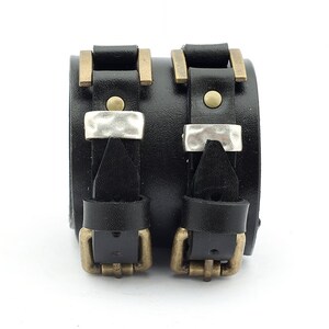 May include: Two black leather bracelets with silver and brass buckles. The bracelets are adjustable and have a distressed look.