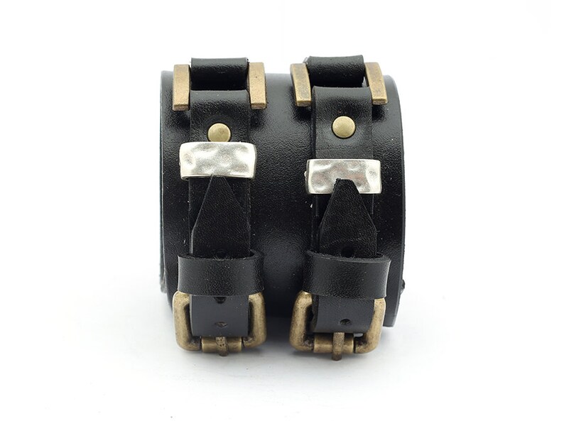 May include: Two black leather bracelets with silver and brass buckles. The bracelets are adjustable and have a distressed look.