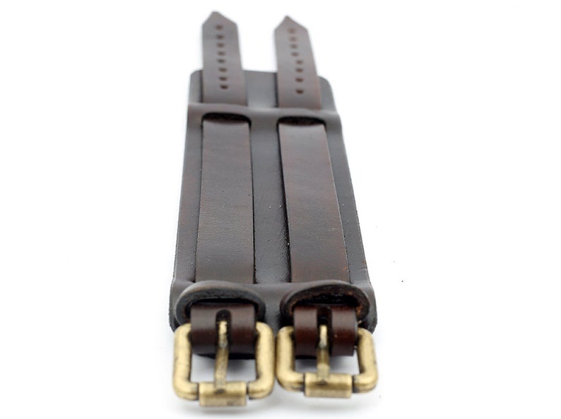 Puede incluir: Un brazalete de cuero marr&oacute;n de doble vuelta con dos hebillas doradas.
