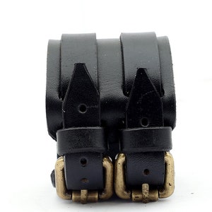 Puede incluir: Un brazalete de cuero negro con doble hebilla y detalles dorados.