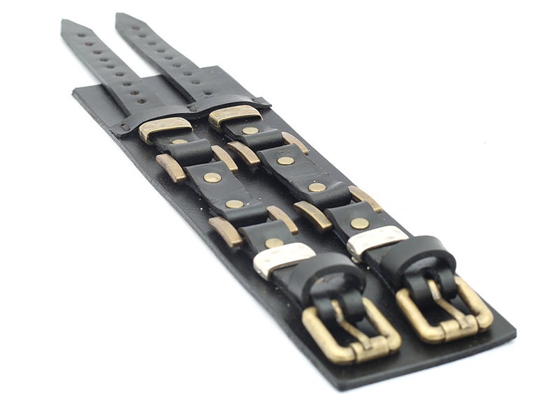 May include: Two black leather bracelets with brass buckles and studs. The bracelets are layered on top of each other.