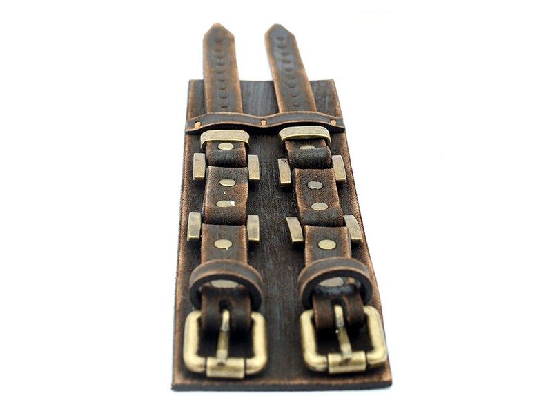 May include: A brown leather cuff bracelet with two buckles and metal accents.