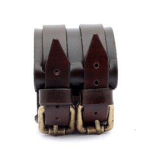 Puede incluir: Dos pulseras de cuero marr&oacute;n con hebillas doradas. Las pulseras est&aacute;n apiladas una encima de la otra.