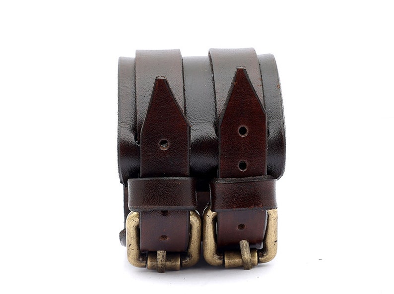 Puede incluir: Dos pulseras de cuero marr&oacute;n con hebillas doradas. Las pulseras est&aacute;n apiladas una encima de la otra.