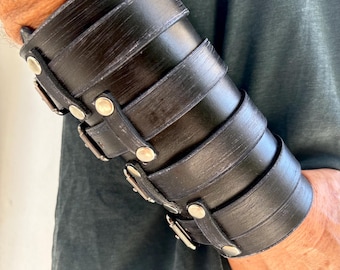May include: Black leather cuff bracelet with silver buckles and rivets. The bracelet is adjustable and has a distressed look.