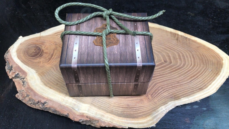 May include: A wooden box with a brown and tan woodgrain pattern, tied with green rope. The box is sitting on a wooden slice.