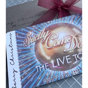 May include: A festive gift set featuring a burgundy ribbon, a grey card, and a ticket for "Strictly Come Dancing: The Live Tour." The ticket displays a disco ball and the text "Merry Christmas."