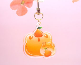 May include: A clear acrylic keychain featuring a cartoon orange with a face and a smaller cartoon cat holding an orange. The keychain has a gold metal clasp.