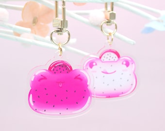 May include: Two pink and white cartoon frog charms with black eyes and a black mouth. The charms are attached to gold keychains.