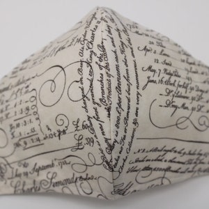 May include: A white fabric face mask with a black and white script pattern. The script includes dates, numbers, and the words "Duty charged on Bey. Ale Gryder Vinegar" and "Branches of the".