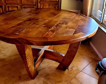 May include: A round wooden table with a unique, curved base. The table top is made of reclaimed wood with a natural finish and features a decorative inlay of turquoise stones.