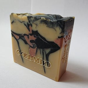 May include: A rectangular bar of soap featuring a marbled design in shades of tan, black, and copper. The word "COLUMIO" is embossed on the front face, and the text "Kyzumi Soap" is vertically embossed along the right side of the bar.