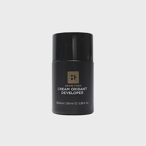 May include: A black bottle of Brow Code Cream Oxidant Developer. The bottle has a black cap and gold lettering. The text on the bottle reads "BROW CODE CREAM OXIDANT DEVELOPER" and "3% 10 vol | 100 ml e 3.38 fl Oz."