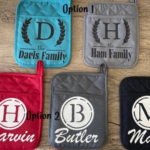 May include: Six different pot holders with personalized designs. Two pot holders have a wreath design with the letter "D" and "H" and the text "the Davis Family" and "the Ham Family". Two pot holders have a circle design with the letter "H" and "B" and the text "Harvin" and "Butler". One pot holder has a circle design with the letter "M" and the text "Major".