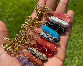 Pode incluir: Uma coleção de acessórios de cabelo com pedras preciosas. Cada pedra tem uma cor diferente e é enrolada em fio de ouro. Os acessórios de cabelo são segurados em uma mão contra um fundo verde.