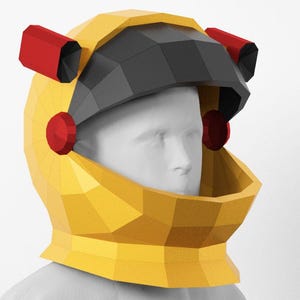 Op de afbeelding: Een gele en zwarte geometrische astronautenhelm met rode accenten. De helm heeft een vizier en twee rode cilinders bovenop. Het ontwerp is hoekig en modern, geschikt voor cosplay of thema-evenementen.