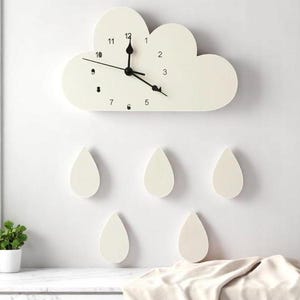 May include: A white cloud-shaped wall clock with black hands and numbers. Below the clock are five white teardrop-shaped decorations, creating a whimsical, weather-themed wall art piece. The clock measures approximately 12 inches across.