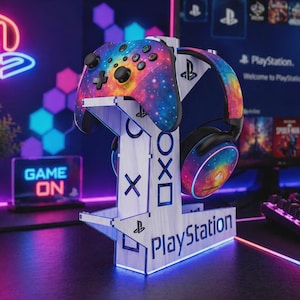 Könnte beinhalten: Ein weißer Holz-PlayStation-Controller- und Headset-Ständer mit einer neonblauen Basis. Der Ständer hält einen Controller und ein Headset im Galaxie-Design. Das Wort "PlayStation" ist auf der Basis aufgedruckt. Der Hintergrund umfasst einen Monitor und eine Tastatur.