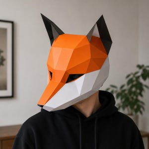 Puede incluir: Una máscara geométrica de zorro con detalles en naranja, blanco y negro. La máscara está hecha de papel o cartulina plegada, con un diseño poligonal. La máscara de zorro se lleva sobre la cara, con aberturas para los ojos visibles.