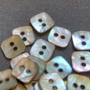 May include: A collection of iridescent, square-shaped buttons with two holes each. The buttons are made of mother of pearl and have a subtle shimmer.