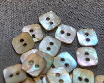 May include: A collection of iridescent, square-shaped buttons with two holes each. The buttons are made of mother of pearl and have a subtle shimmer.