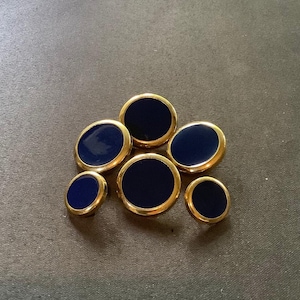 May include: Six round, navy blue buttons with gold trim. The buttons are arranged in a cluster.