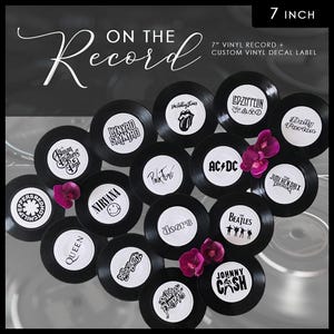 May include: Black 7-inch vinyl records with custom decal labels featuring iconic bands like The Beatles, Nirvana, and AC/DC. The records are arranged with pink flowers, and the text "ON THE Record" is displayed.
