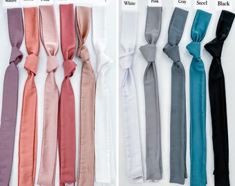 May include: A collection of satin hair scarves in various colors, including mauve, dusty rose, dusty pink, old rose, champagne, ivory, white, light pink, metallic gray, steel, and black. Each scarf is knotted at the top and has a long, flowing tail.
