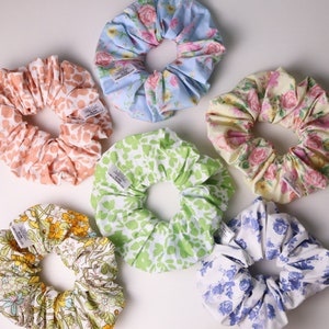May include: Six colorful scrunchies with floral patterns. Each scrunchie has a white tag with the text "BLINK CREATIONS CO."