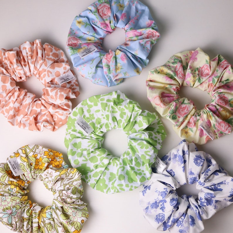 May include: Six colorful scrunchies with floral patterns. Each scrunchie has a white tag with the text "BLINK CREATIONS CO."