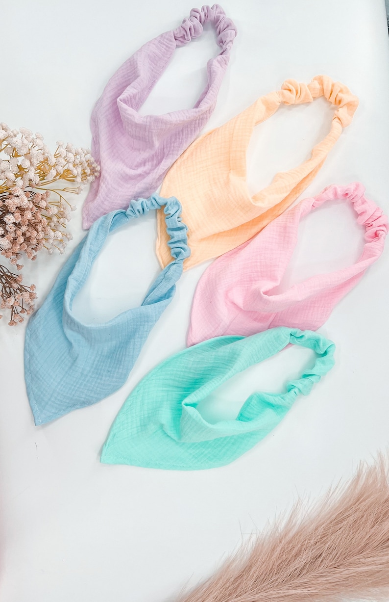 May include: Four fabric headbands in pastel colors: light blue, light pink, light yellow, and light green. Each headband has a gathered elastic band.