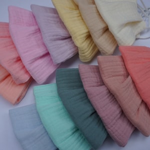 May include: A collection of soft, pastel-colored fabric hats. The hats are in shades of peach, pink, lavender, yellow, and green. Each hat has a textured, crinkled appearance and a drawstring. The hats are likely for babies or children.