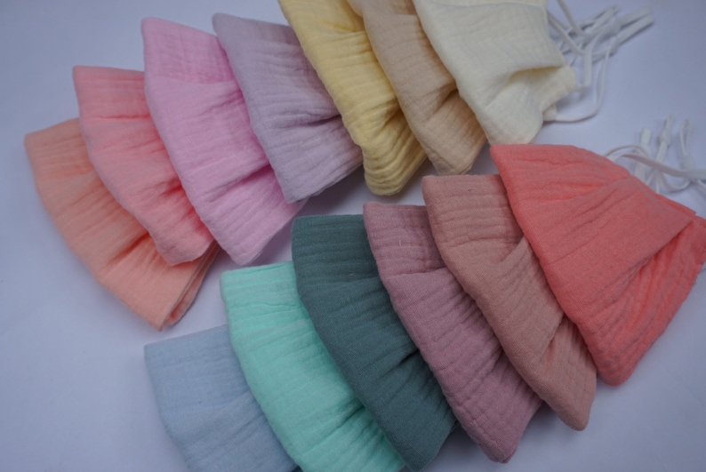 May include: A collection of soft, pastel-colored fabric hats. The hats are in shades of peach, pink, lavender, yellow, and green. Each hat has a textured, crinkled appearance and a drawstring. The hats are likely for babies or children.