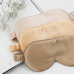 May include: Three silk sleep masks in different shades of beige. The masks are arranged in a stack, with the lightest shade on top and the darkest shade on the bottom.