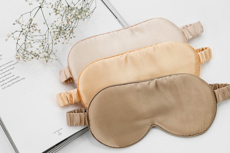 May include: Three silk sleep masks in different shades of beige. The masks are arranged in a stack, with the lightest shade on top and the darkest shade on the bottom.