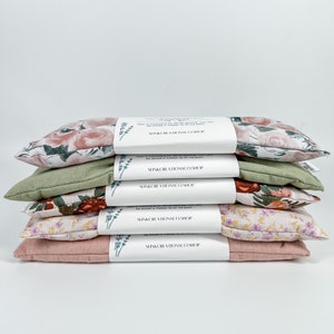 May include: A stack of five floral eye pillows, each with a different pattern. The pillows are all pink, green, and white. The pillows are labelled "SunKissed Aromas Co. Shop".