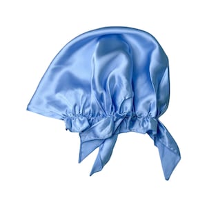 Puede incluir: Un gorro para dormir de satén azul claro con la parte superior fruncida y un lazo en la parte posterior.