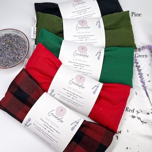 May include: Five lavender eye pillows in different fabric colours: black, pine green, green, red, and plaid. Each pillow is labelled "Lavender Eye Pillow" and filled with flax seed and organic lavender flowers. The pillows are arranged in a row from top to bottom.