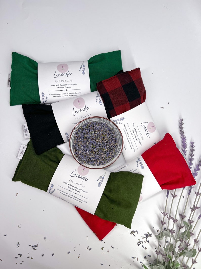 May include: Assortment of six lavender eye pillows in various colours, including green, black, red, and plaid. The pillows are filled with flax seed and organic lavender flowers. The text on the label reads "Lavender Eye Pillow".