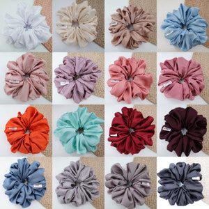 May include: A collection of 12 different colored satin scrunchies. The scrunchies are arranged in a grid pattern on a light brown background. Each scrunchie is made of a different color satin fabric, including white, beige, light brown, pink, purple, light blue, orange, turquoise, red, gray, dark gray, and blue.